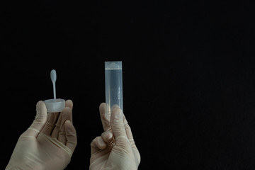 Female hands in white sterile medical gloves hold a lid and a sterile white plastic container or jar for stool analysis or coprology test on a black background. Horizontal close-up