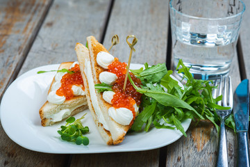 Classic breakfast, hot sandwich with red salmon caviar and mozzarella on a plate on a wooden table.