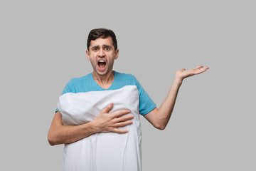 Tired brunet man in a blue tee resting on a white pillow isolated over grey background.