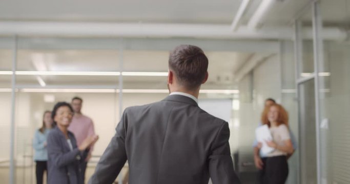 Backside view of overjoyed company chief walking through office room and throwing his jacket. Office staff congratulating male boss with signing great deal and giving him high five.