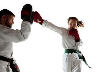 Junior in kimono practicing hand-to-hand combat with coach, martial arts. Young female mongol fighter with green belt training on white studio background. Concept of healthy lifestyle, sport, action.