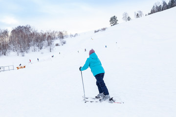 Fototapeta na wymiar A woman skier slides down the Altai mountain over white snow in a sports tourist base Turquoise Katun. Seasonal sports.