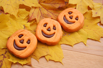  Halloween cookies in shape of a pumpkin filled with choocolate on wooden table with yellow leaves