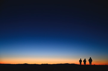 Three tourist walking in morning mountains. Sunrise colors in background