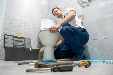 man plumber in uniform repairing toilet bowl using instrument kit professional repair service