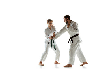 Junior in kimono practicing hand-to-hand combat with coach, martial arts. Young female mongol fighter with green belt training on white studio background. Concept of healthy lifestyle, sport, action.