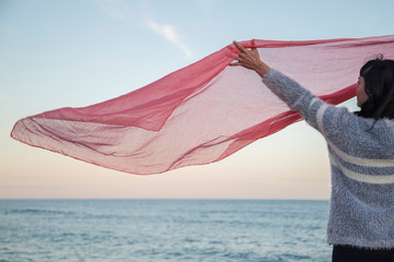 Fototapeta na wymiar Woman holding a pink scarf to the wind in the sea.
