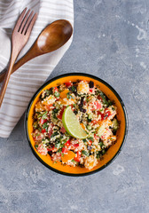 Tabouleh: vegetable couscous salad. Vegetables and couscous salad tabouleh in the orange ceramic bowl on concrete surface. Fresh summer salad with lime slice, wooden spoon, fork and white linen towel