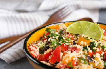 Tabouleh: vegetable couscous salad Vegetables and couscous salad tabouleh in the orange ceramic bowl on concrete surface. Fresh summer salad with lime slice, wooden spoon, fork and white linen towel