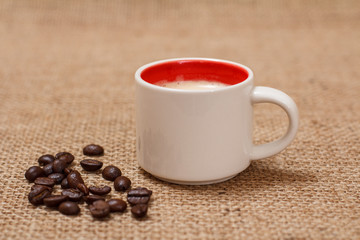Cup of coffee and roasted coffee beans on sackcloth.