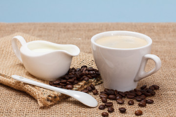 Cup of coffee, cream and coffee beans on sackcloth