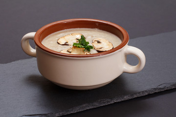 Cream soup with mushrooms in porcelain bowl on black background.
