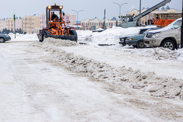 clearing compacted snow from the road using heavy snow removal equipment and a grader