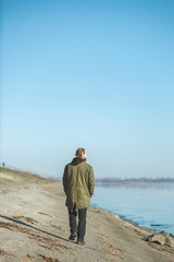 Rear view of a bearded man in a warm jacket standing against a misty river in sunny morning sunrise