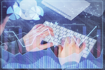 Double exposure of graph with man typing on computer in office on background. Concept of hard work.