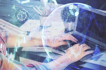 Double exposure of stock graph with businessman typing on computer in office on background. Concept of hard work.