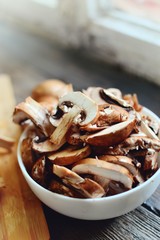 Royal fresh mushrooms on a wooden background. Sliced ​​champignons in a white bowl. Cooking process. Vertical view 