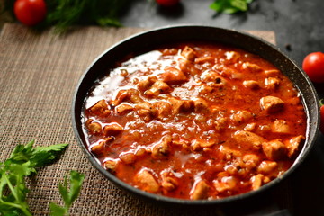 Indian food. Chicken Tikka Masala in a pan on a dark background. Appetizing meat with curry and tomato sauce, gravy with various spices. Delicious food, vertical view from the side.