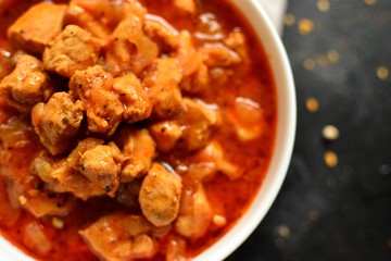 Indian food. Chicken Tikka Masala in a white bowl on a dark background. Appetizing meat with curry and tomato sauce, gravy with various spices. Tasty food, close-up, top view