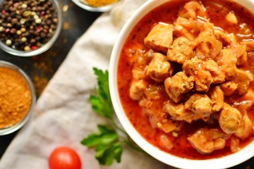 Tikka Masala. Chicken in tomato sauce in a white bowl. Spices and cherry tomatoes with parsley. Tasty chicken meat on a dark background. Horizontal view
