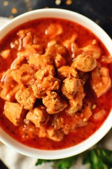 Indian food. Chicken Tikka Masala in a white bowl on a dark background. Appetizing meat with curry and tomato sauce, gravy with various spices. Tasty food, close-up, top view