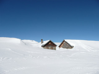 Huts in deep snow on the Alps under sunny sky - with copy-space