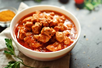 Tikka Masala. Chicken in tomato sauce in a white bowl. Spices and cherry tomatoes with parsley. Tasty chicken meat on a dark background. 