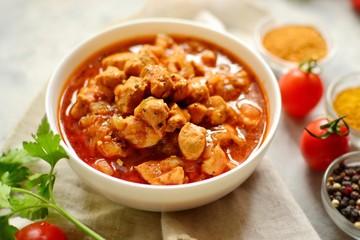 Indian food. Chicken Tikka Masala in a white bowl on a dark background. Appetizing meat with curry and tomato sauce, gravy with various spices. Tasty food, close-up, top view