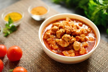 Tikka Masala. Chicken in tomato sauce in a white bowl. Spices and cherry tomatoes with parsley. Tasty chicken meat on a dark background. 