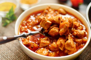 Indian food. Chicken Tikka Masala in a white bowl with spoon, on a dark background. Appetizing meat with tomato sauce, gravy. Food close up 