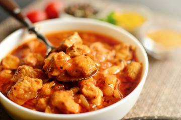 Indian food. Chicken Tikka Masala in a white bowl with spoon, on a dark background. Appetizing meat with tomato sauce, gravy. Food close up 