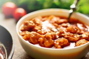 Indian food. Chicken Tikka Masala in a white bowl with spoon, on a dark background. Appetizing meat with tomato sauce, gravy. Food close up 