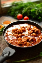 Indian food. Chicken Tikka Masala in a pan on a dark background. Appetizing meat with curry and tomato sauce, gravy with various spices. Delicious food, vertical view from the side.