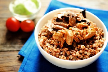 Buckwheat porridge in a white bowl. Buckwheat porridge with mushrooms and chicken breast. Wooden background and blue textile, linen napkin in blue.