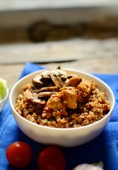 Buckwheat porridge in a white bowl. Buckwheat porridge with mushrooms and chicken breast. Wooden background and blue textile, linen napkin in blue.