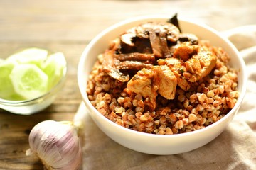 Buckwheat porridge in a white bowl. Buckwheat porridge with mushrooms and chicken breast. Wooden background and linen napkin.
