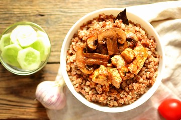 Buckwheat porridge in a white bowl. Buckwheat porridge with mushrooms and chicken breast. Wooden background and linen napkin. Top view 
