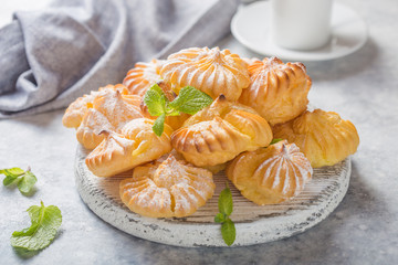 Profiterole or gougeres, eclair with custard cream filling served for breakfast on a white plate with tea on a concrete table, view from above, close-up