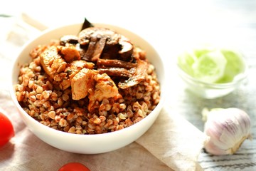Buckwheat porridge in a white bowl. Buckwheat porridge with mushrooms and chicken breast. Wooden background and linen napkin.