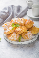 Profiterole, or gougeres or eclair with custard cream filling served for breakfast on a white plate with tea on a concrete table, view from above, close-up