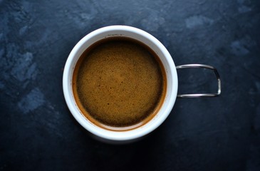 Natural coffee in a white cup. Coffee top view. Coffee with cream on a dark, dark blue background. Place for text.