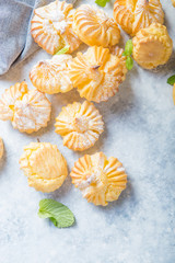 Profiterole or gougeres or eclair with custard cream filling served for breakfast on a white plate with tea on a concrete table, view from above, close-up