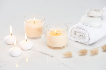 Fototapeta na wymiar fluffy bunny tail grass near burning white candles in glass and rolled towel with stones on marble white surface