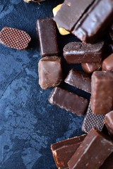 Assortment of chocolates. Candies on a dark bluish background. Top view place for text. Dark chocolate. Chocolate bars.