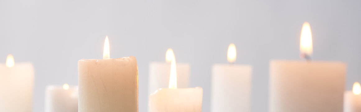 selective focus of burning white candles glowing isolated on grey, panoramic shot