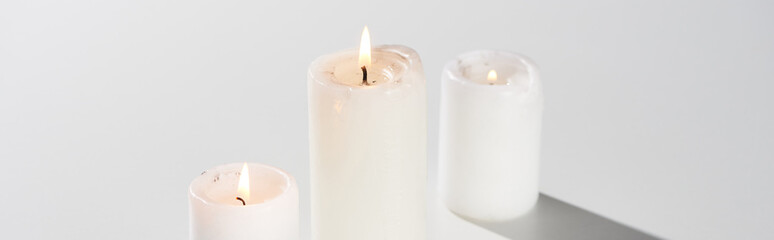 Fototapeta na wymiar burning candles glowing on white background with shadow, panoramic shot