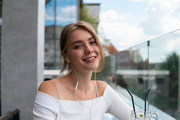 Porteait of blond woman blogger with cocktail is listening music or e-book on smartphone connected...