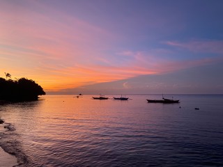 Incredibly beautiful, magical sunset, sunrise in the tropics with shades of pink, purple, blue, orange, yellow color. A calm sea with dark boats on the horizon against the sky and clouds.