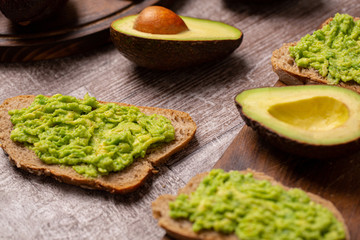 Avocado sandwiches next to cutted ones on wooden board
