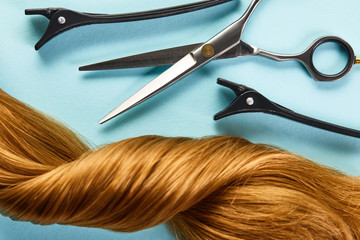 Top view of clamps and scissors with twisted brown hair on blue background